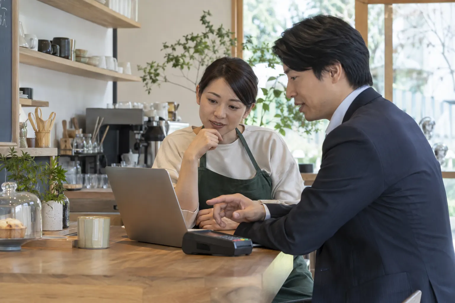 日本の小さな店舗で、パソコンと決済端末を確認する相談風景（イメージ）